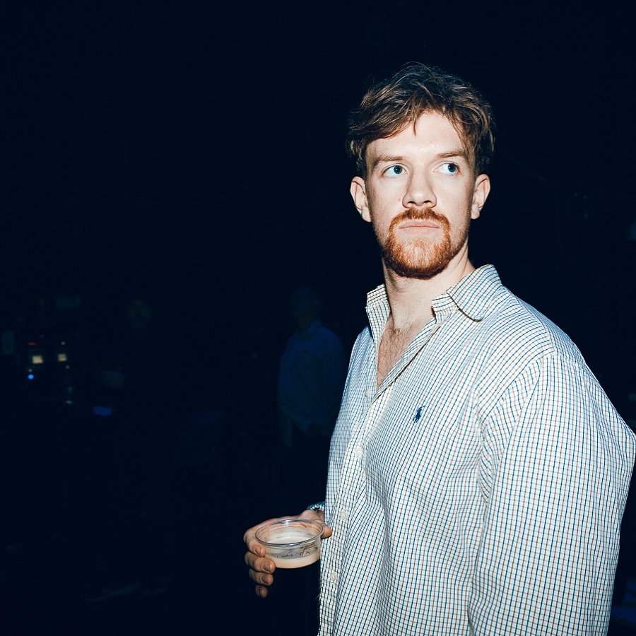 Oisín McCaffrey backstage in a checked shirt, holding a drink