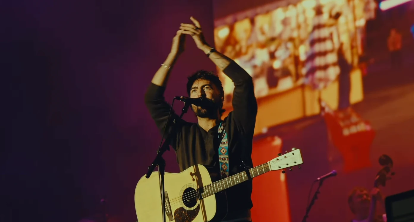 Robbie Cunningham on stage with an acoustic guitar, arms raised above his head
