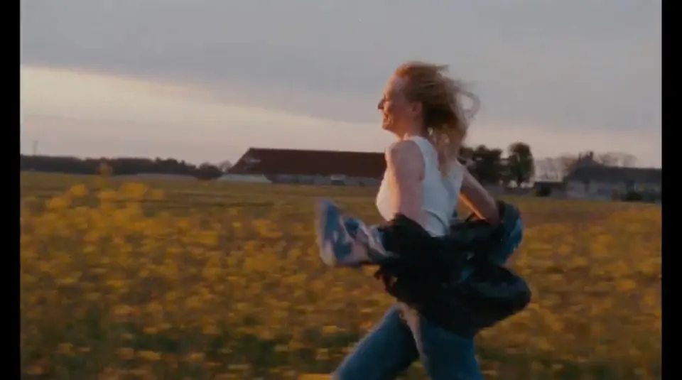A woman running through a yellow field at dusk, still from the Moral Victory music video