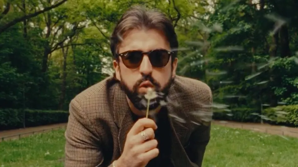 A man in sunglasses blowing a dandelion, still from The Swell music video