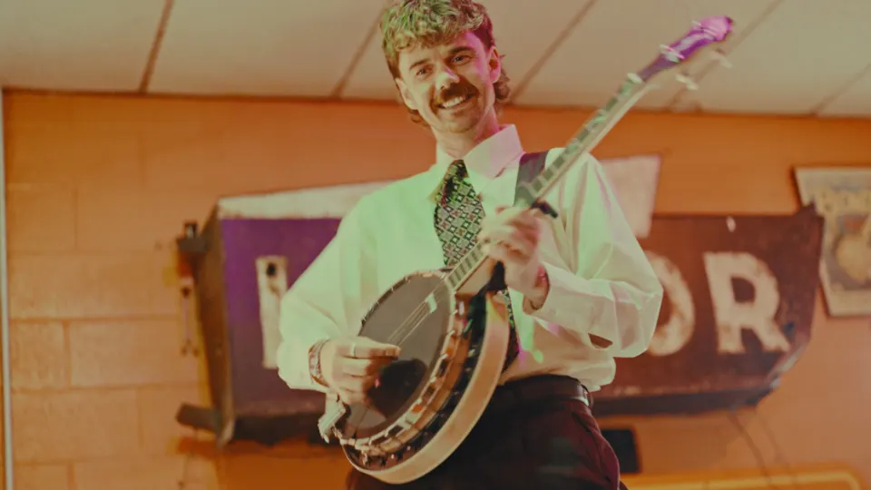 A banjo player grinning in a diner, still from the Last Rites music video
